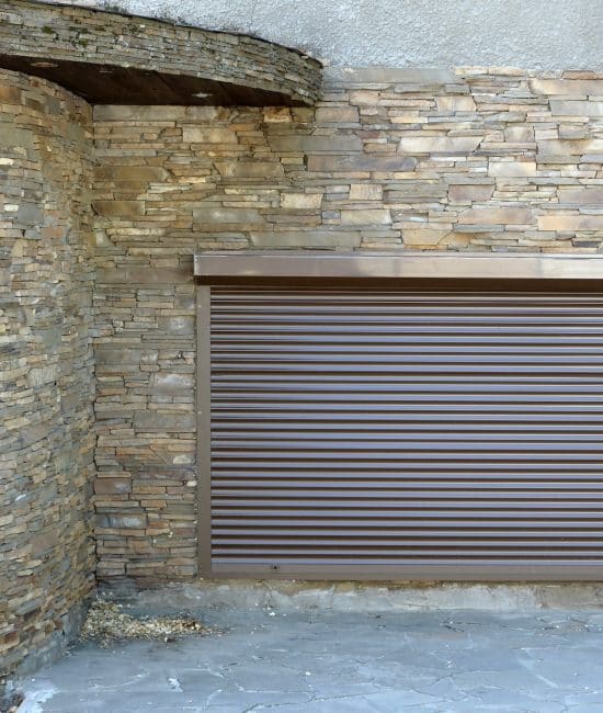 A window with brown metal rolling shutters and wall decoration with artificial stone