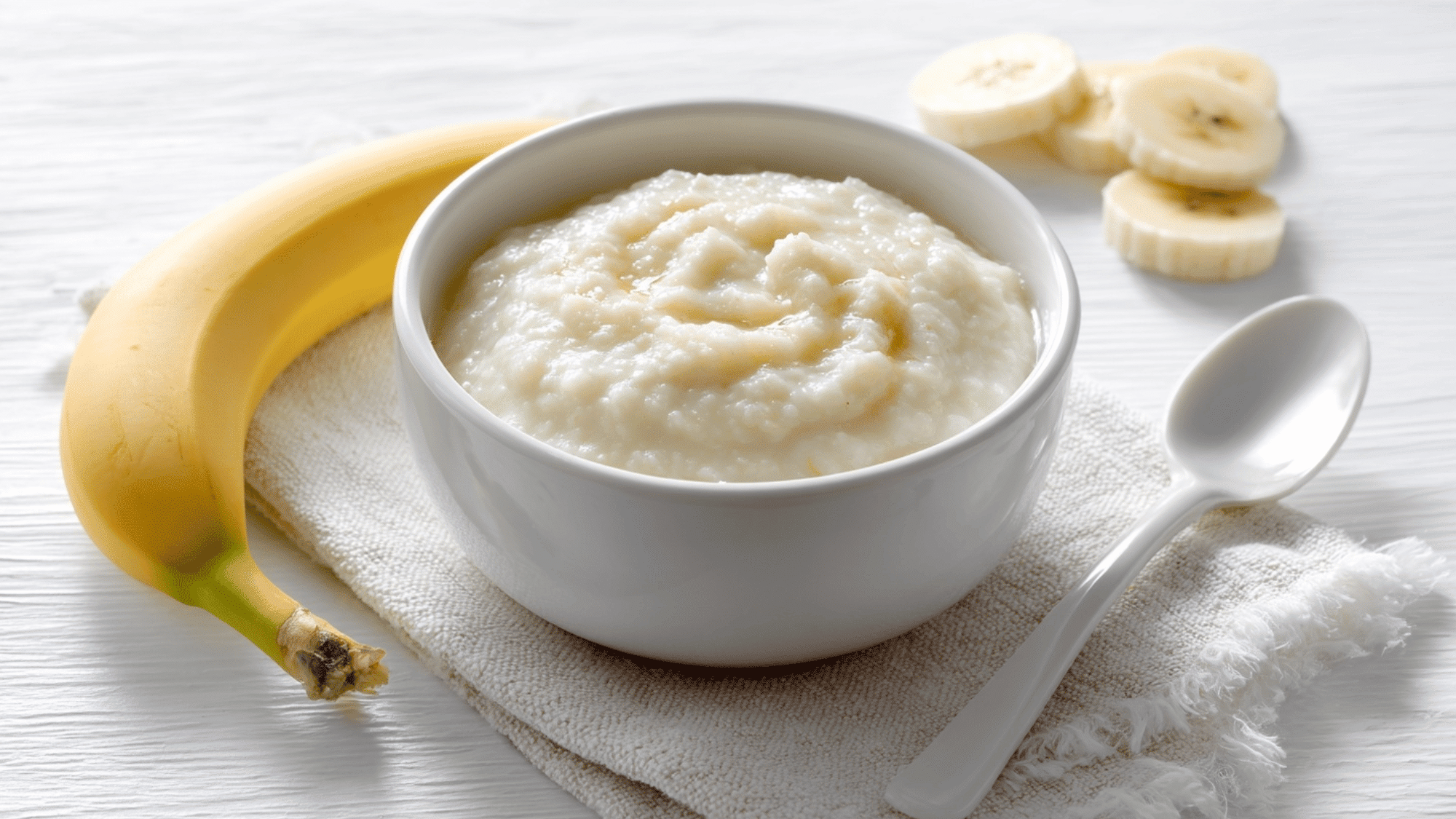Baby cereal with mashed banana in a bowl on a clean white background