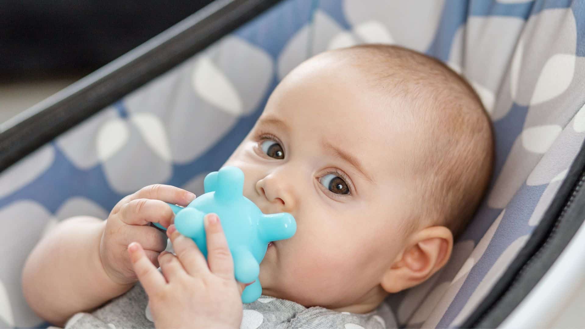 Baby chewing a teething toy while lying in a stroller, showing common teething behavior linked to molars in toddlers and gum discomfort during molar eruption