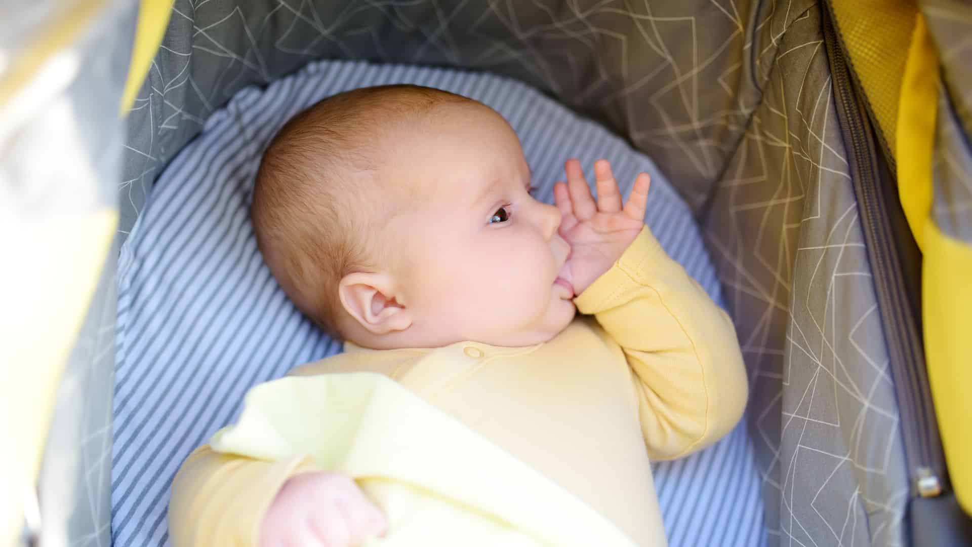 Baby lying in crib sucking thumb, a natural self soothing behavior often encouraged when learning how to teach baby to self soothe