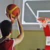 Boy taking a jump shot toward the hoop during basketball games practice on an indoor court, focusing on shooting skills and accuracy