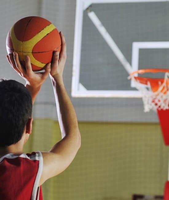 Boy taking a jump shot toward the hoop during basketball games practice on an indoor court, focusing on shooting skills and accuracy