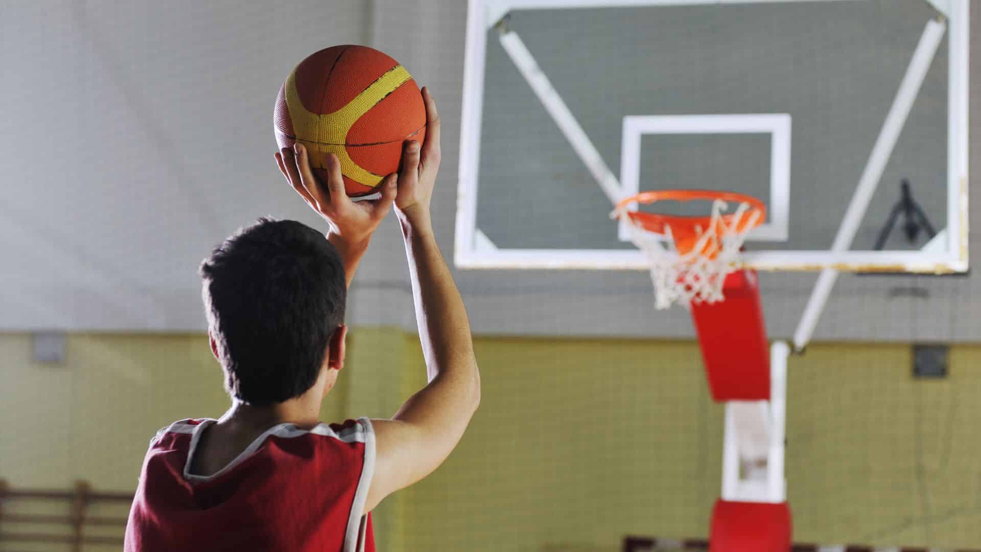 Boy taking a jump shot toward the hoop during basketball games practice on an indoor court, focusing on shooting skills and accuracy