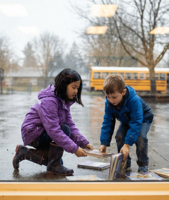 Child helping a friend pick up books that dropped on the floor