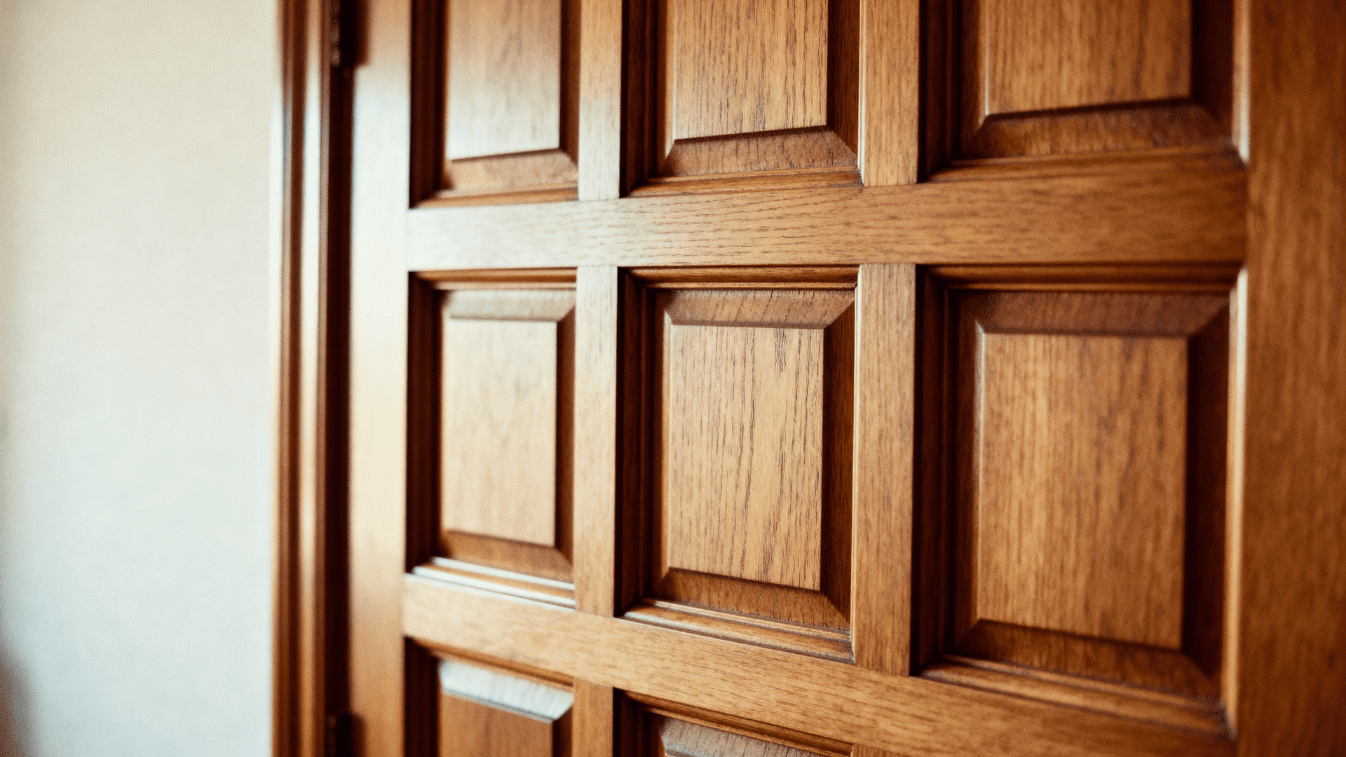 Close-up of a wooden paneled door with a grid of square recessed panels, showing warm tones, smooth finish, and detailed craftsmanship.