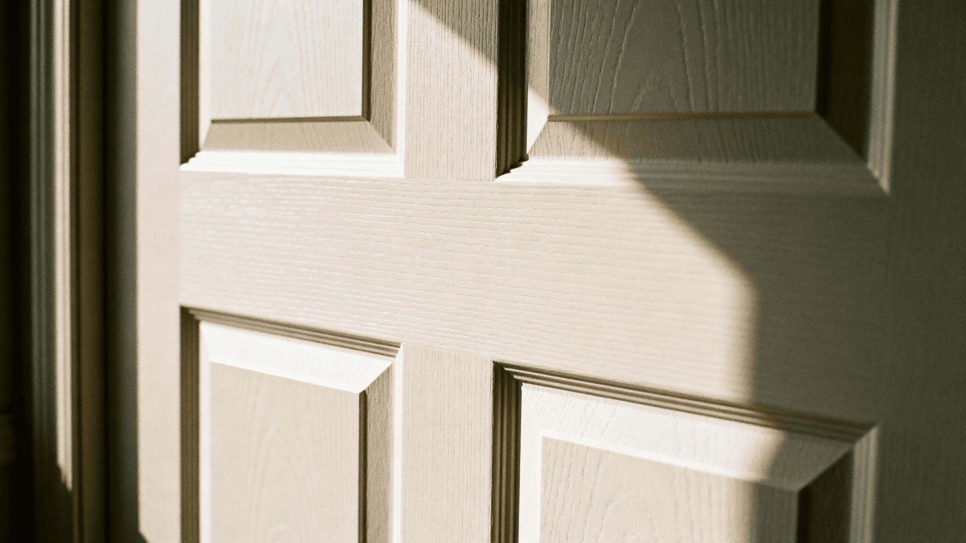 Close-up of painted moulded panel door with raised detailing, soft sunlight casting shadows across textured surface and clean design