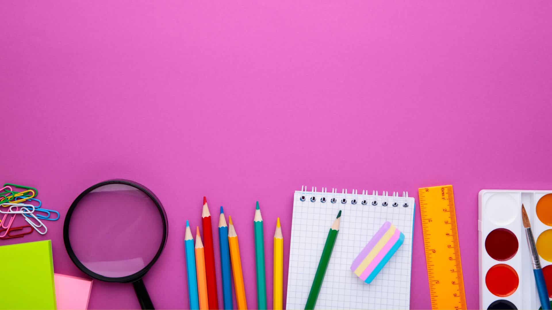 Colorful school supplies including pencils, notebook, ruler, and paints arranged on pink background for kindergarten homeschool curriculum setup