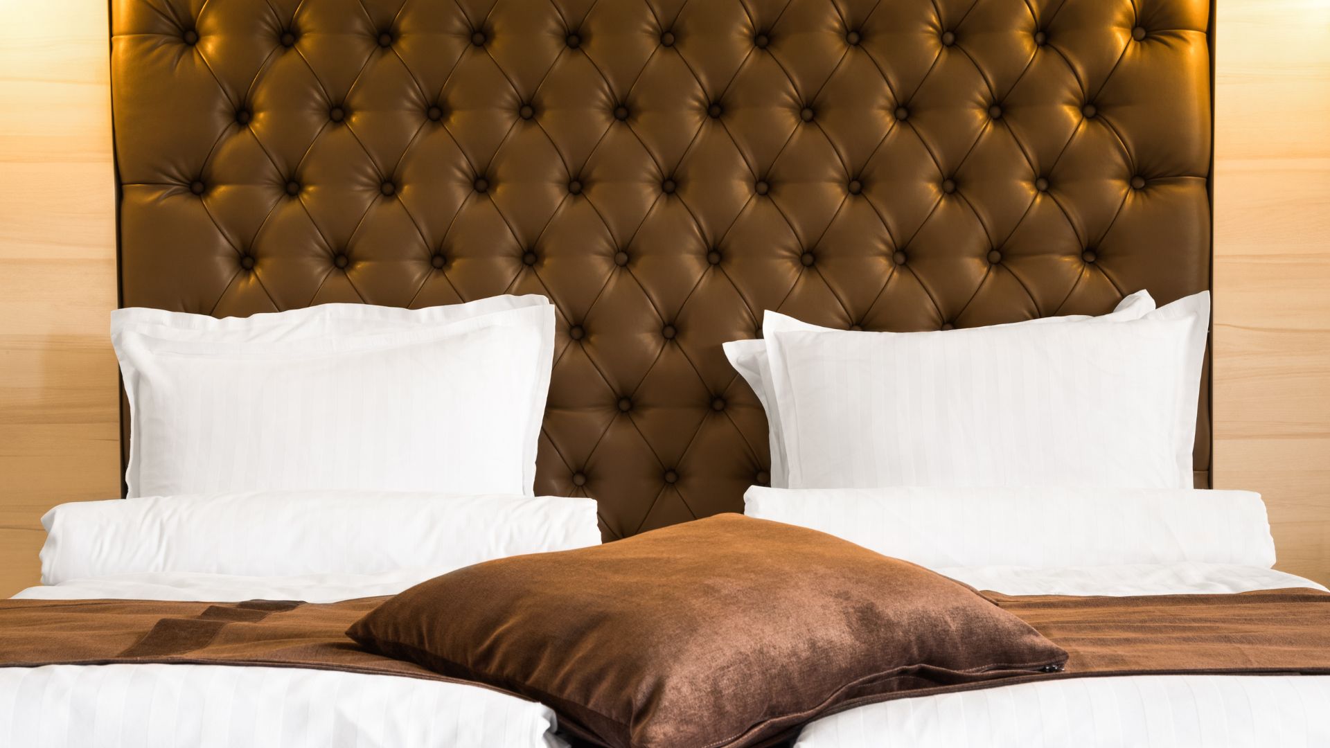 DIY upholstered headboard with brown tufted leather design, diamond button detailing, and white bedding in a modern bedroom setting