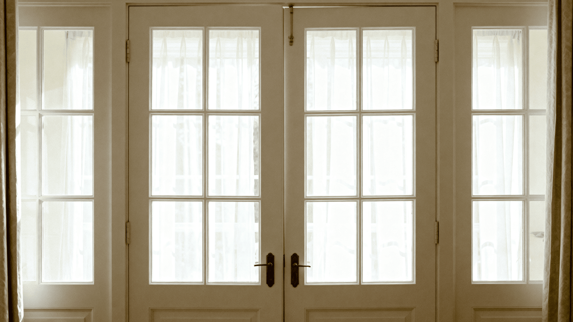 Elegant French double doors with glass panes, soft curtains behind, and warm light creating a bright, classic interior look