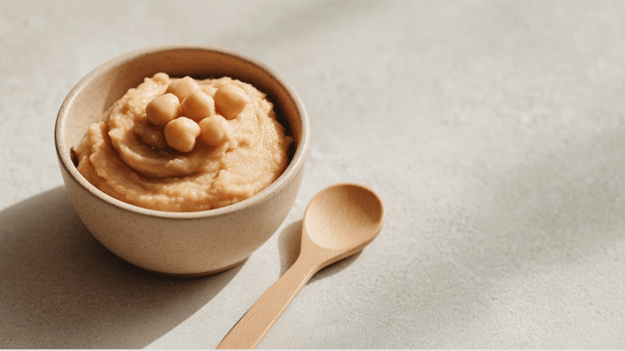Mashed chickpeas in a baby bowl with spoon on a clean kitchen counter