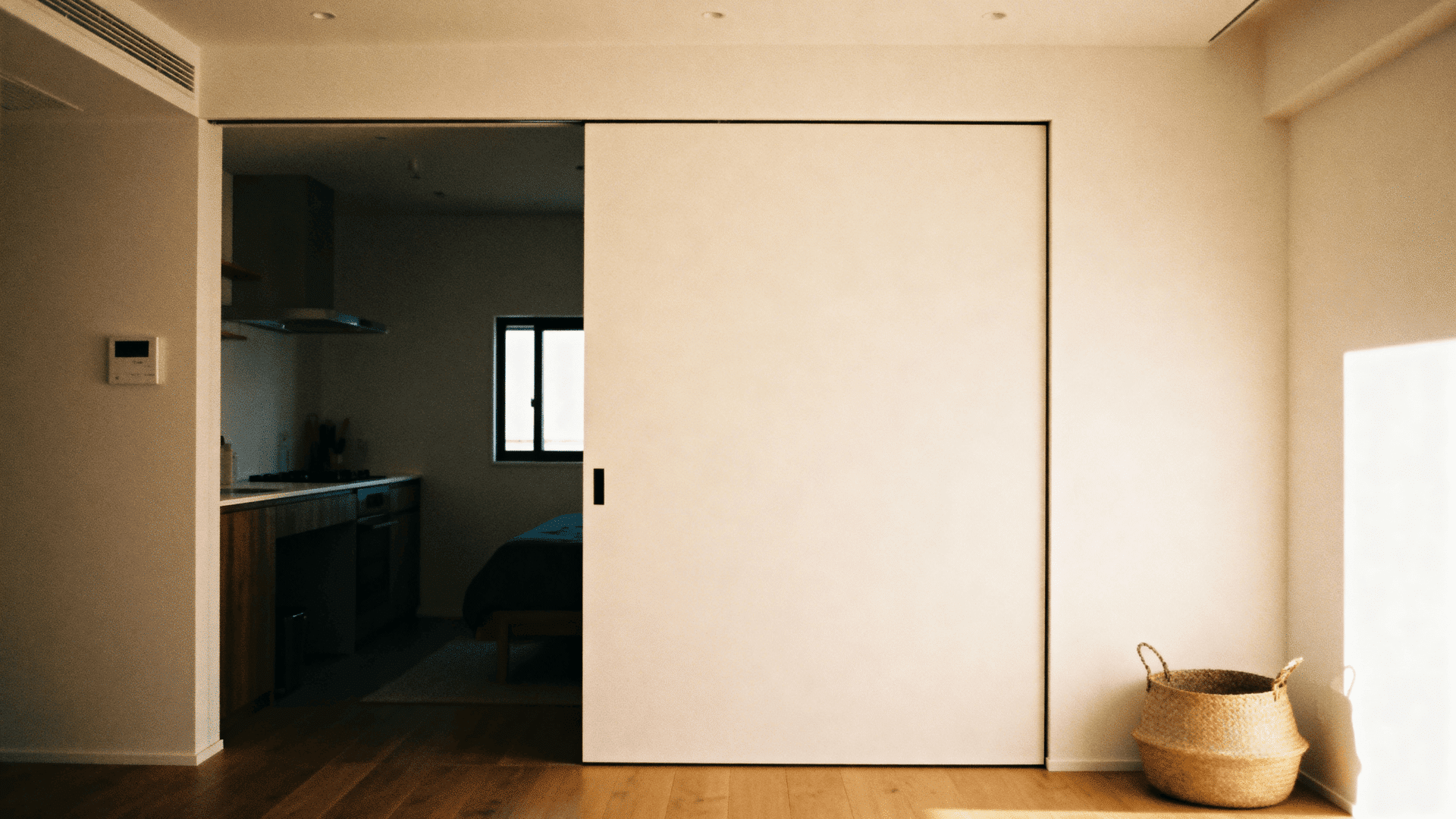 Minimalist pocket sliding door partially open, revealing a cozy bedroom and kitchen, with warm lighting and clean modern interior design
