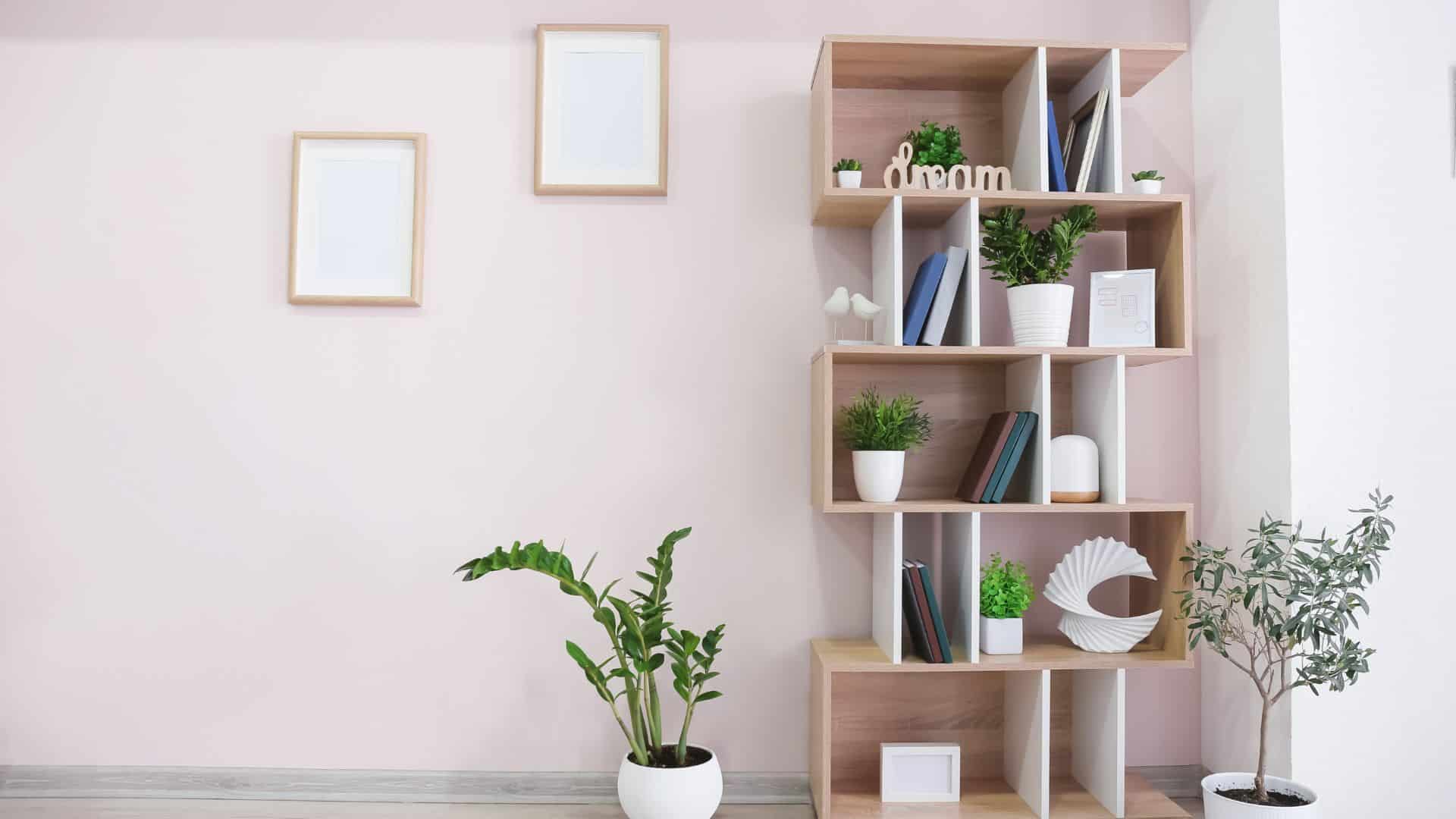 Modern DIY bookshelves made from wooden cube shelves styled with books, plants, and decor against a soft pink wall in a minimalist living space