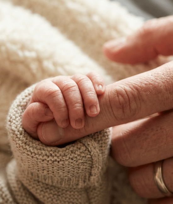 Newborn baby tightly gripping an adult finger showing strong grasp reflex