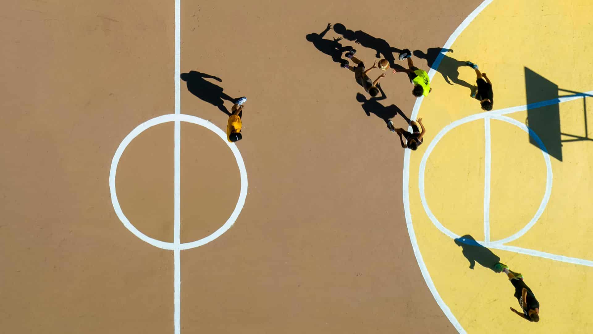 Overhead view of kids playing basketball games on an outdoor court, dribbling and passing near the hoop during a casual pickup game.