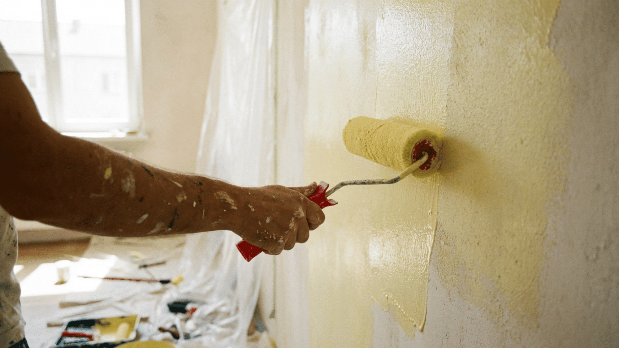 Painter applying second coat of latex paint on smooth wall in bright room