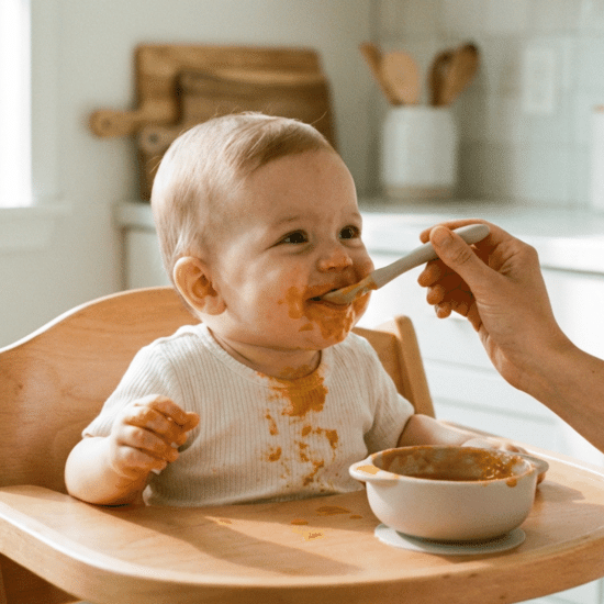 Parent feeding baby puree in a high chair during first solid food stage