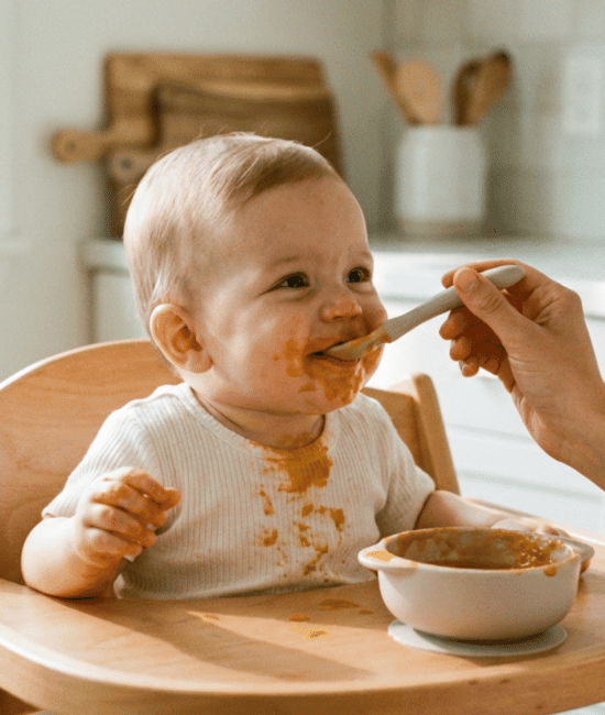 Parent feeding baby puree in a high chair during first solid food stage