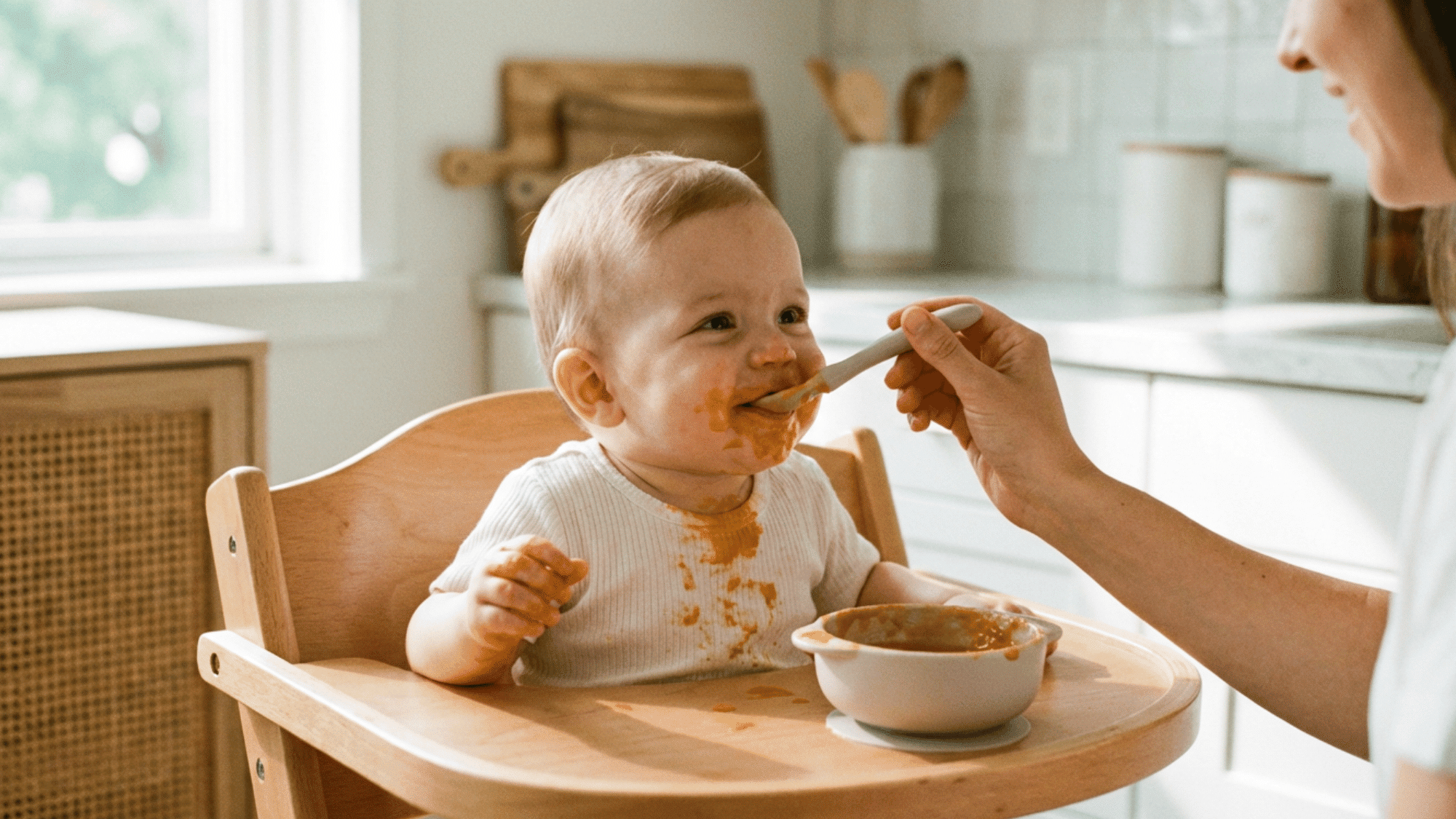 Parent feeding baby puree in a high chair during first solid food stage