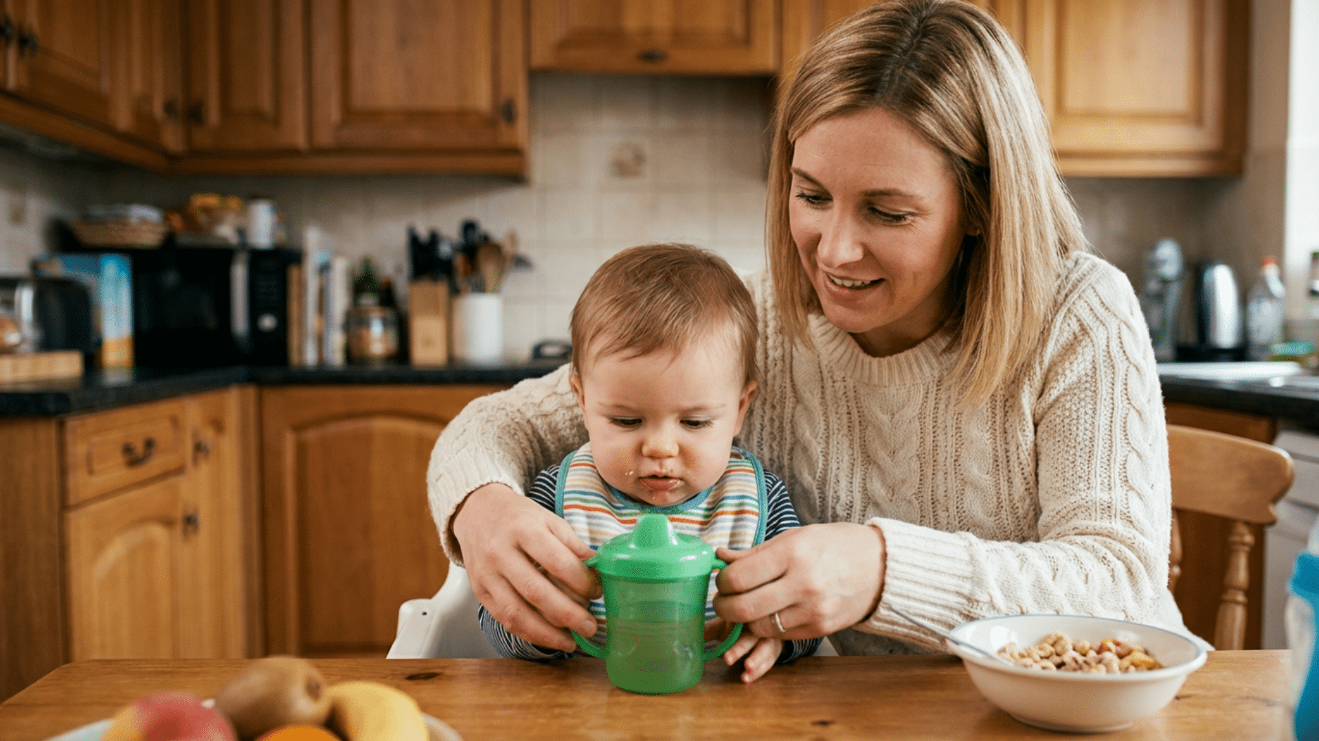 Parent helping baby learn to drink from a sippy cup