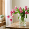 Pink tulips drooping slightly in a glass vase near a window with soft natural light.