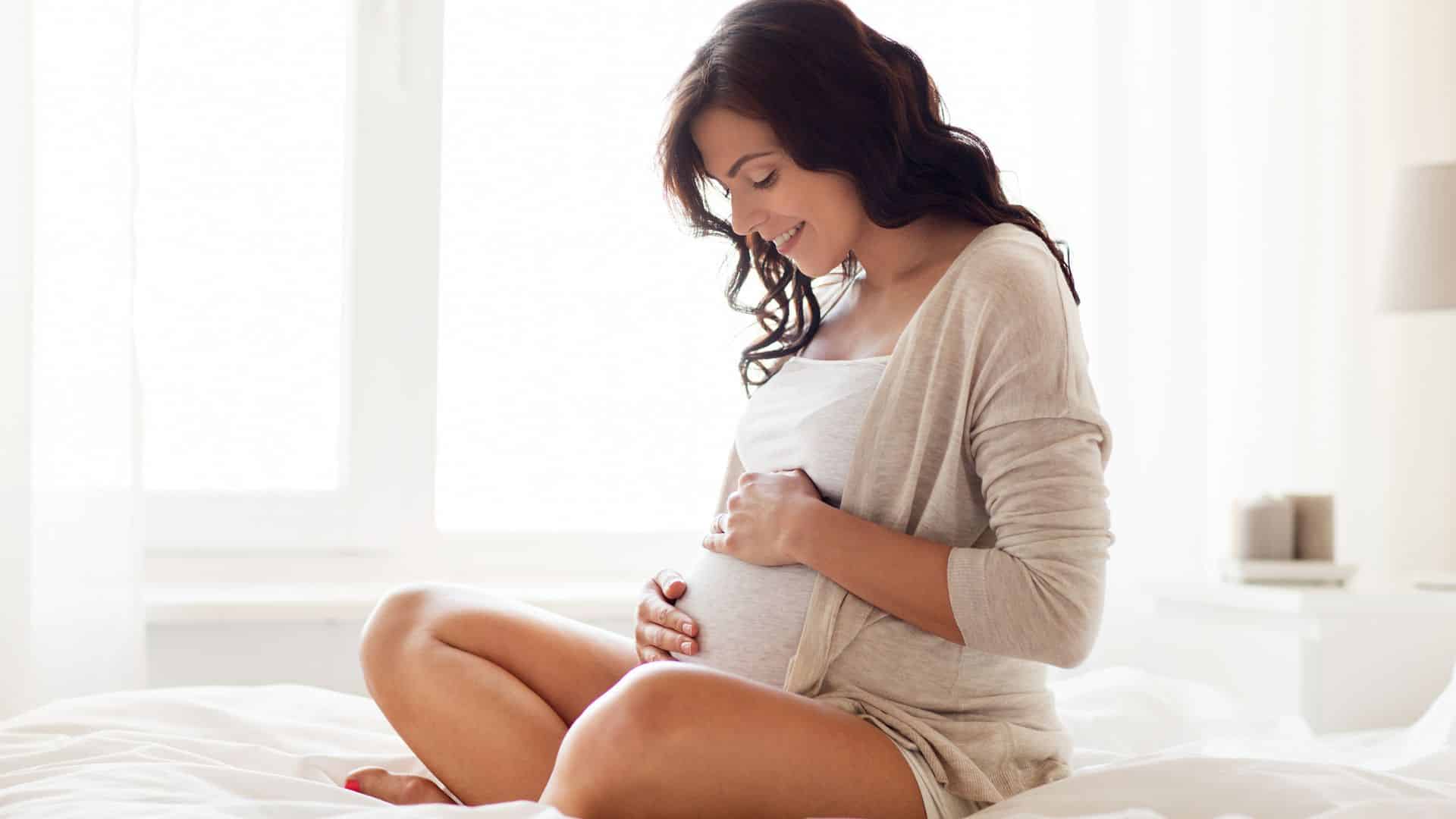 Pregnant woman gently holding her baby bump at home, illustrating when is the second trimester and early pregnancy growth stages