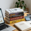 Stack of personal finance books on a desk with laptop, notebook and coffee
