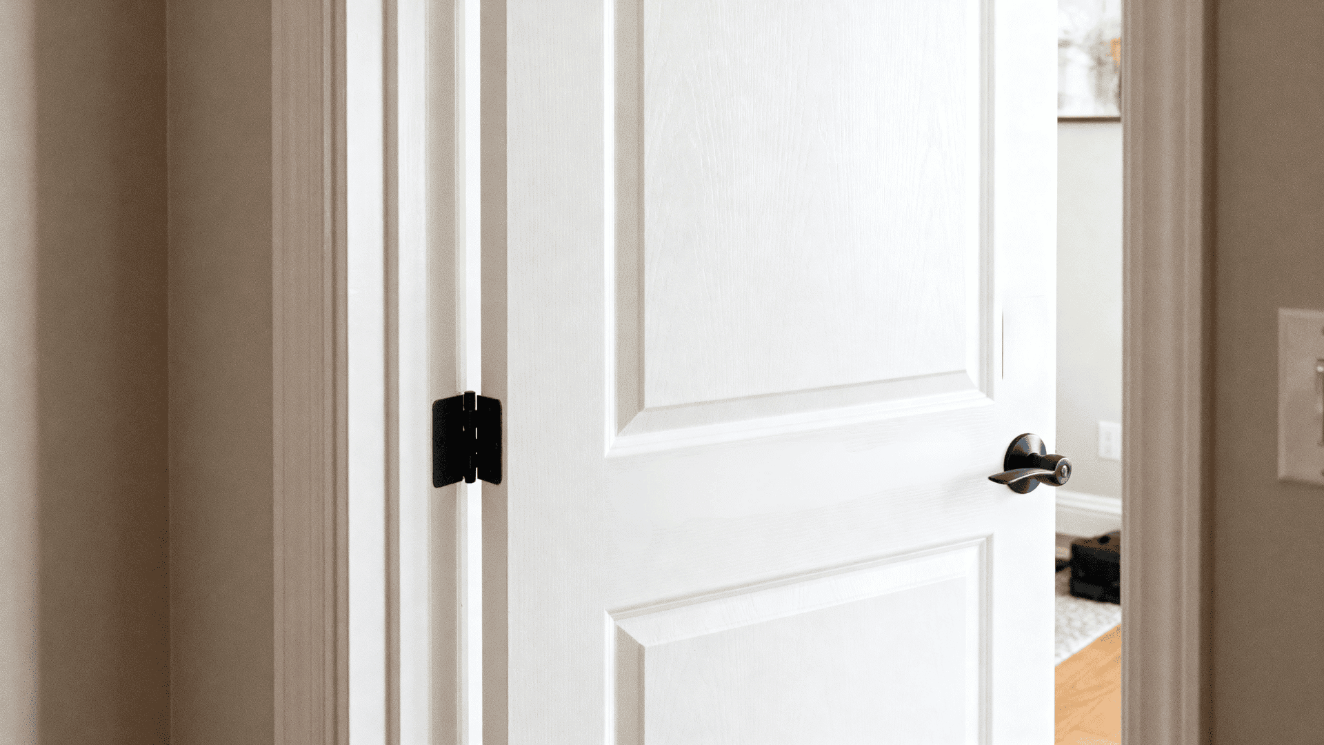 _White interior door slightly open with visible left-side hinges and black handle, showing door swing direction in a bright home setting