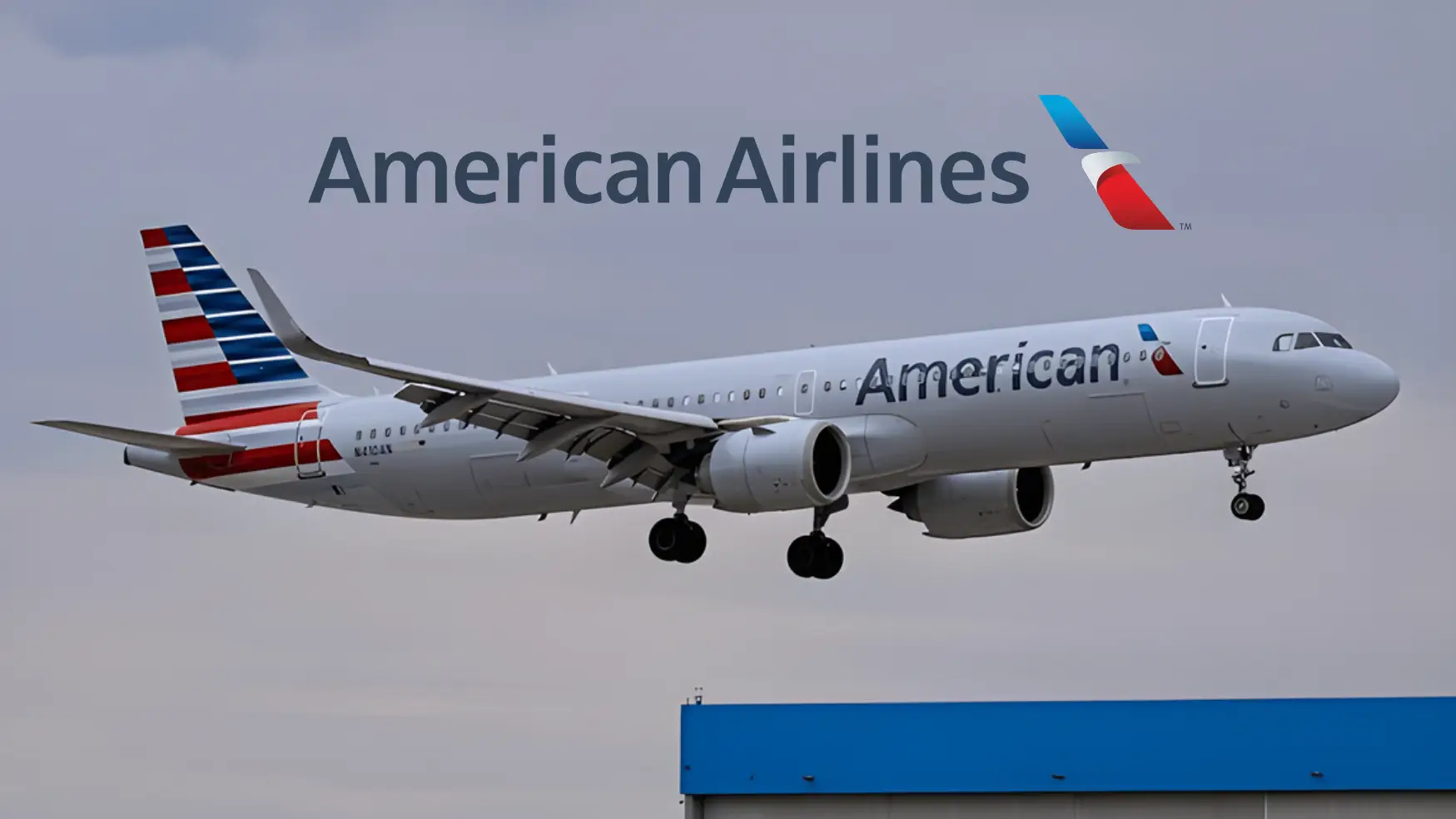 American Airlines plane landing against cloudy sky with hangar roof visible below