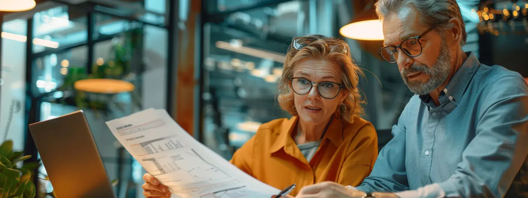 Two people reviewing financial documents in modern office with warm lighting