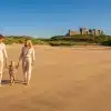 Family walking on sandy beach with castle on hill in background under clear blue sky
