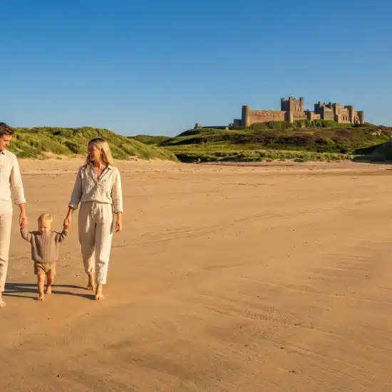 Family walking on sandy beach with castle on hill in background under clear blue sky