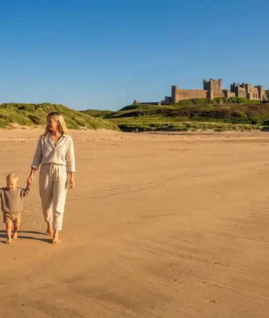 Family walking on sandy beach with castle on hill in background under clear blue sky