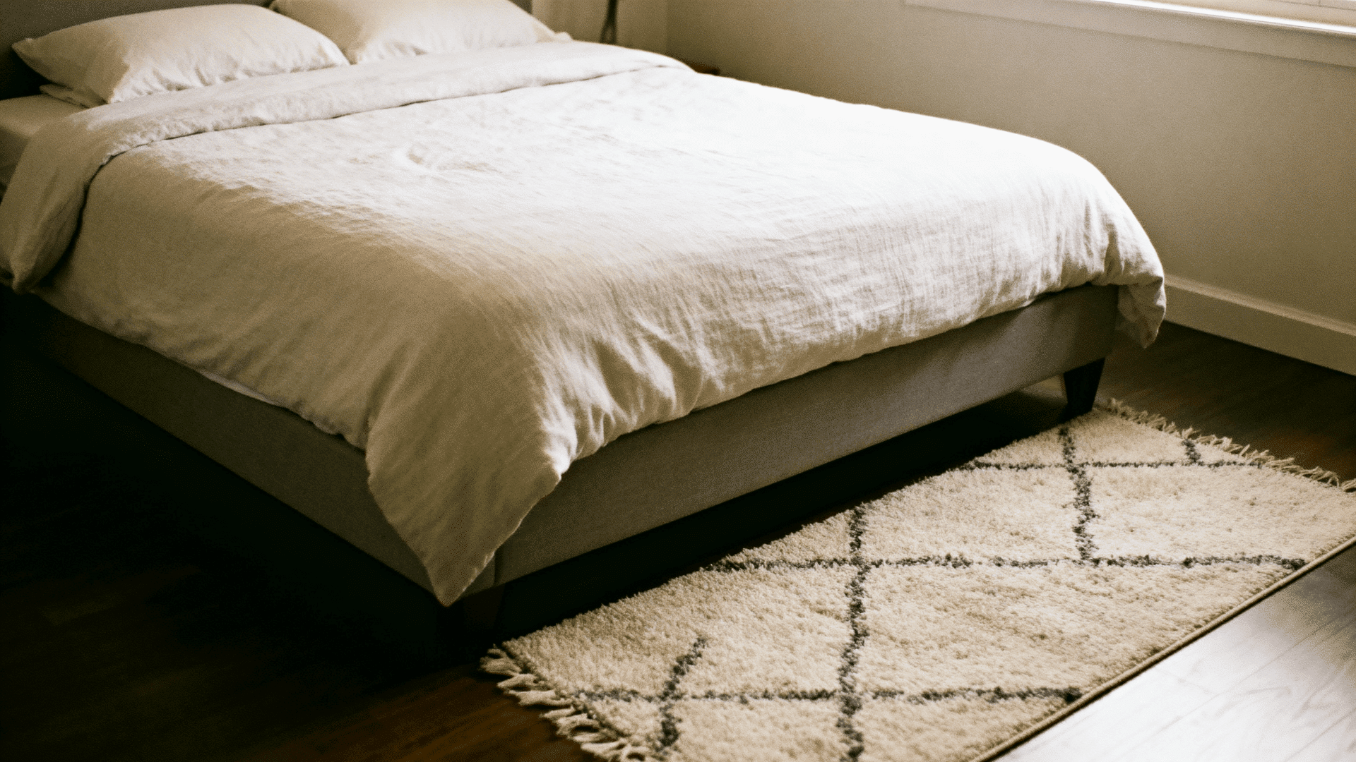 5x7 rug placed under a queen bed, extending around the sides and foot, in a small cozy bedroom with neutral tones and natural light.