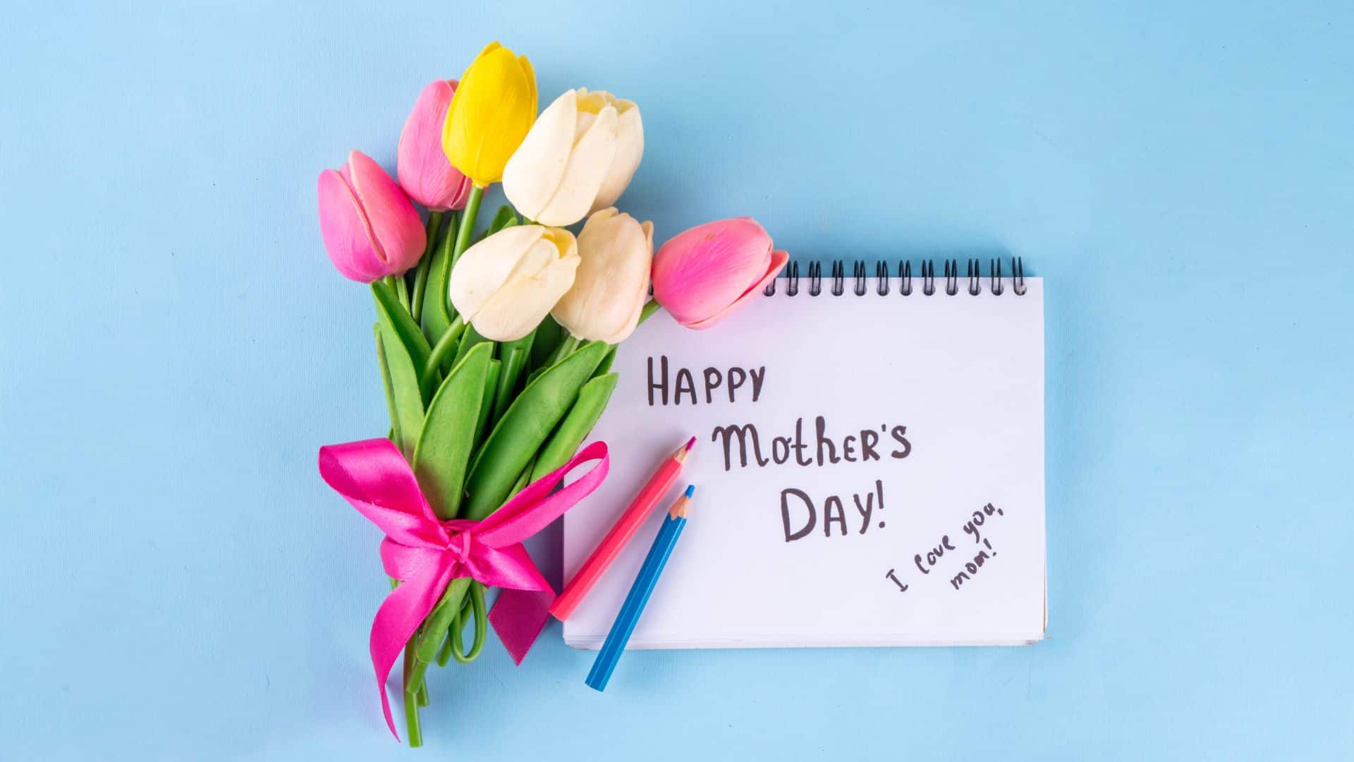 A Mother's Day card with 'Happy Mother's Day!' and 'I love you, mom!' written inside a notebook, paired with a colorful tulip bouquet