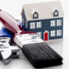 A miniature dark blue house sits behind a red-handled paintbrush and a silver adjustable wrench on a white reflective surface.