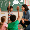 Kids raise hands eagerly as teacher smiles in colorful classroom, question marks on board, encouraging curiosity and active participation