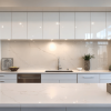 Modern white kitchen featuring glossy handleless cabinetry, a marble-look quartz backsplash and island countertop.
