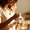 Mother mixing baby formula in a bottle at home kitchen, warm natural light, preparing infant feeding with calm nurturing atmosphere