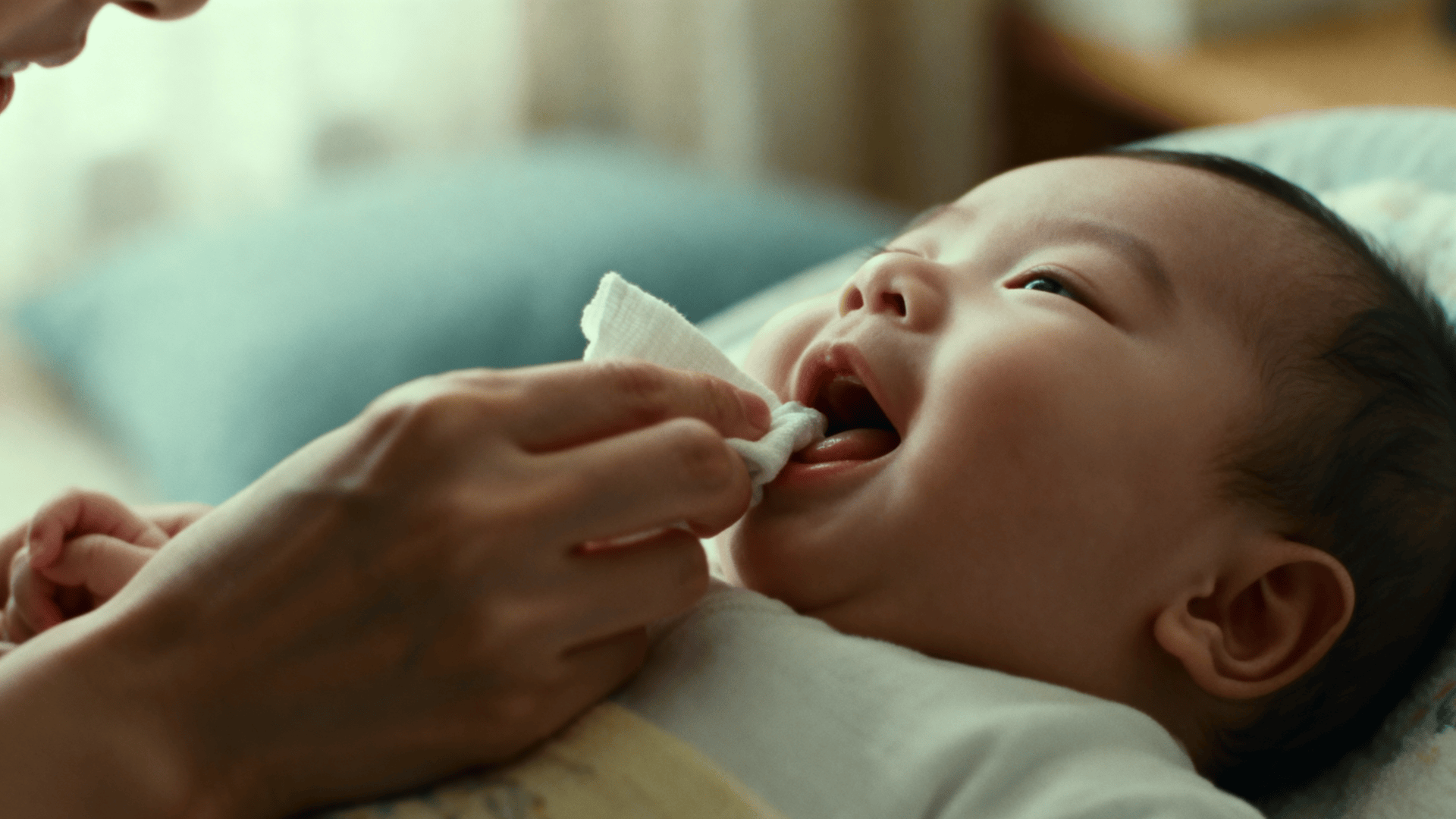 Parent gently cleaning a baby’s gums with a soft cloth, showing early oral care routine in a calm, nurturing home setting.