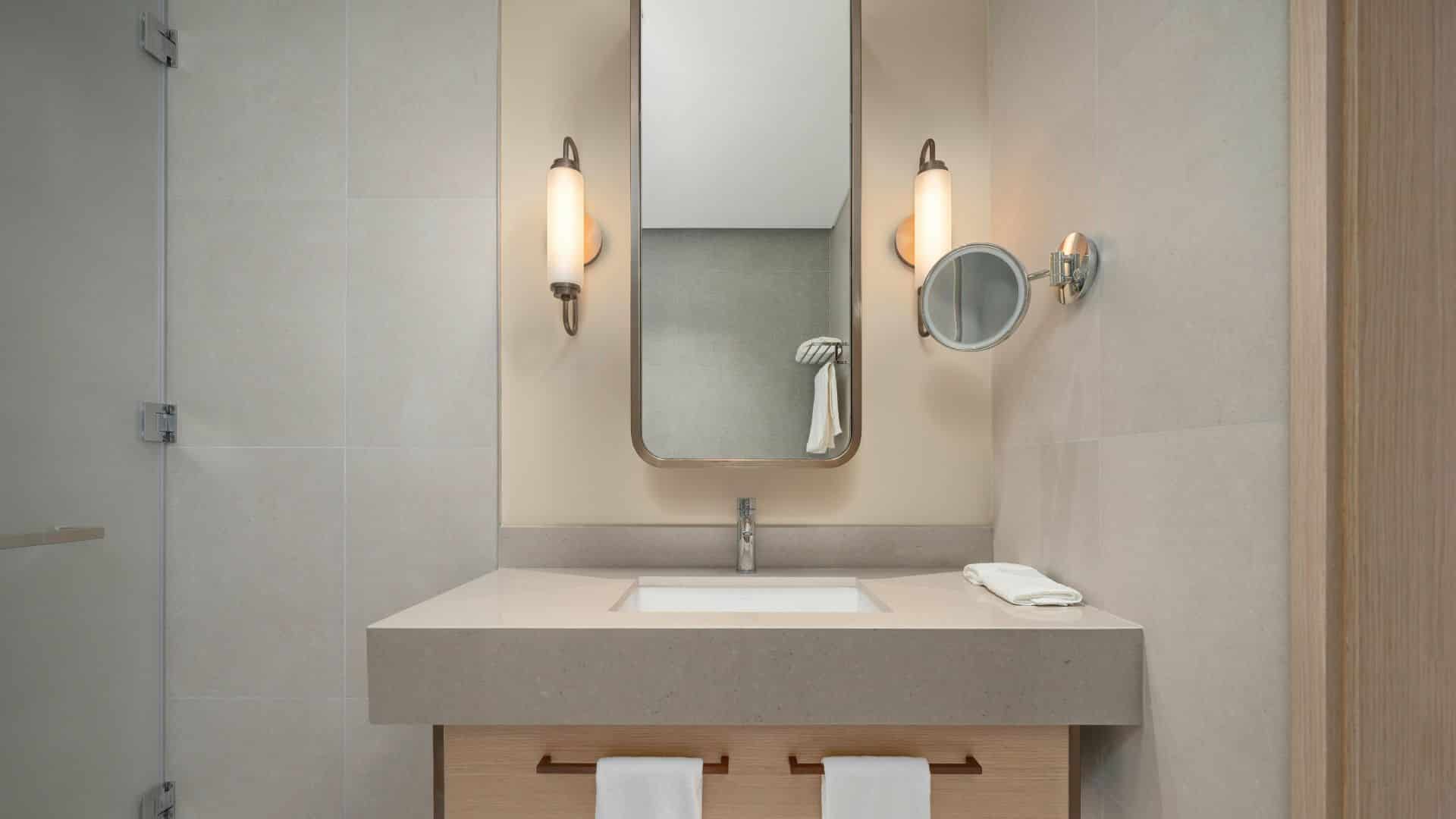 Vanity mirror size guide showing a wall-mounted rectangular mirror above a single sink vanity with side lighting in a modern bathroom setup