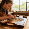 Woodworker carving detailed pattern into wooden tray in bright workshop, focused craftsmanship with tools and natural light