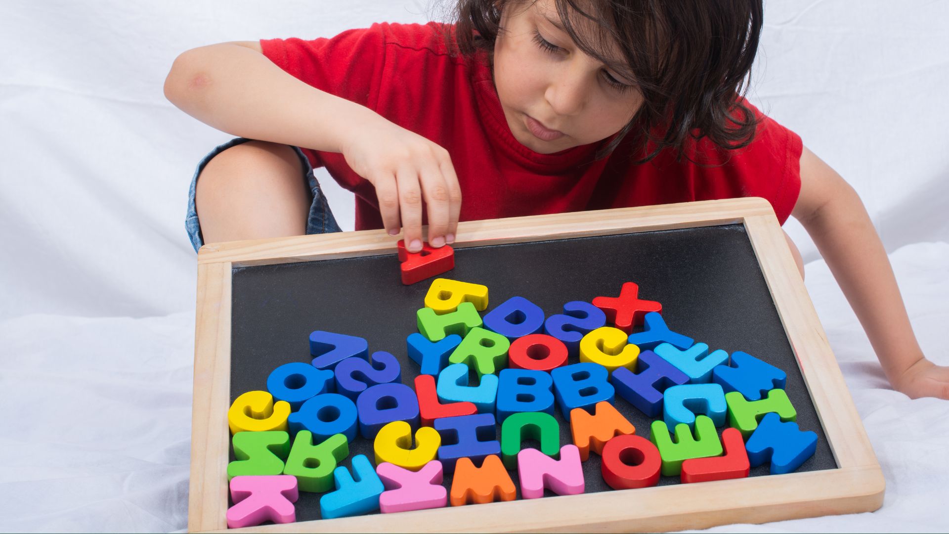 A child playing with colorful alphabet magnets on a chalkboard, demonstrating the alphabetic principle through letter recognition and manipulation