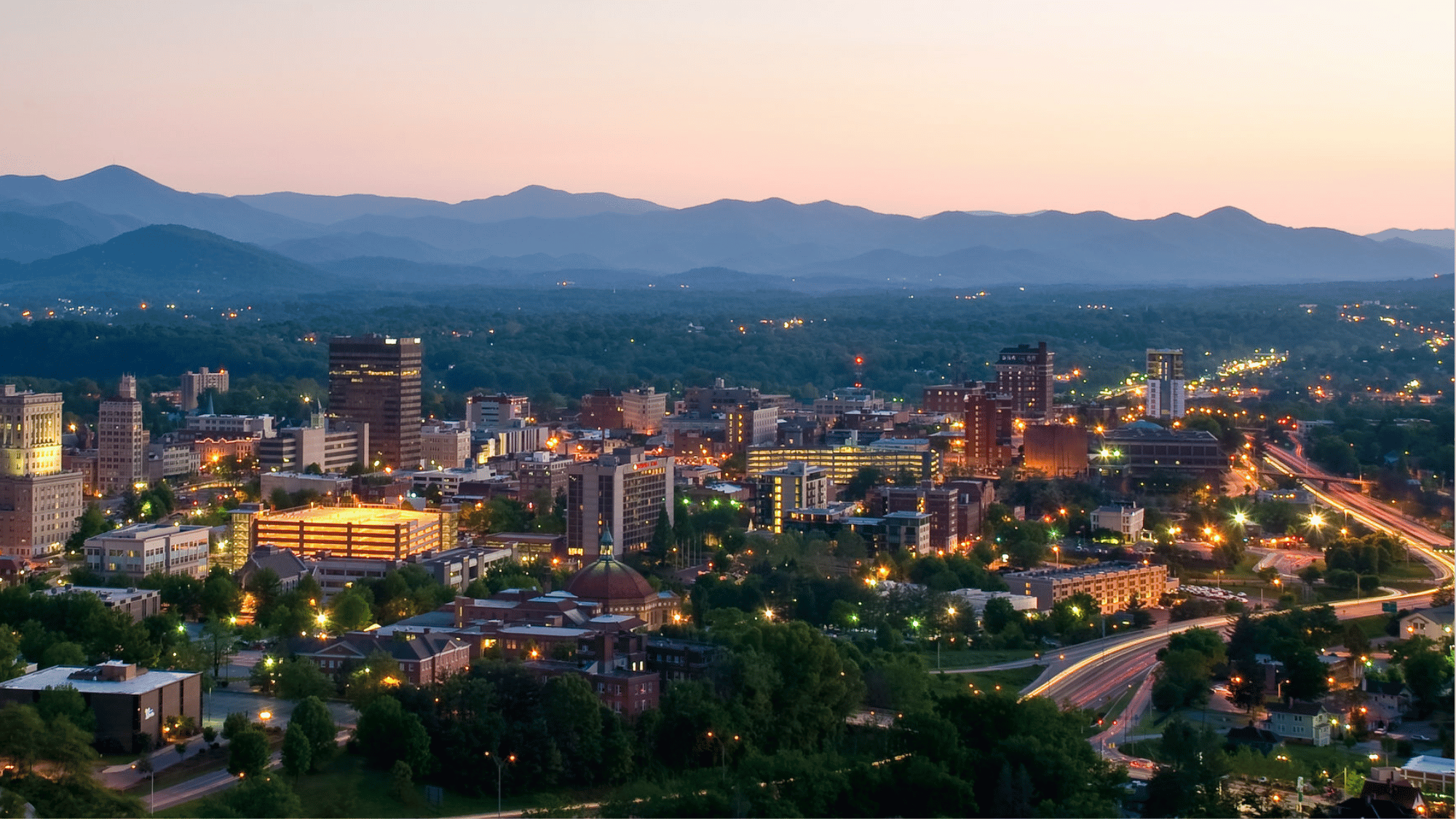 Asheville North Carolina skyline at dusk with Blue Ridge Mountains and glowing city lights
