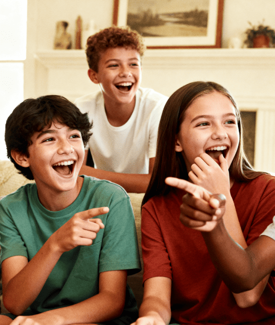 Group of kids laughing, pointing, and playing a fun game together on a couch in a bright, cozy living room setting