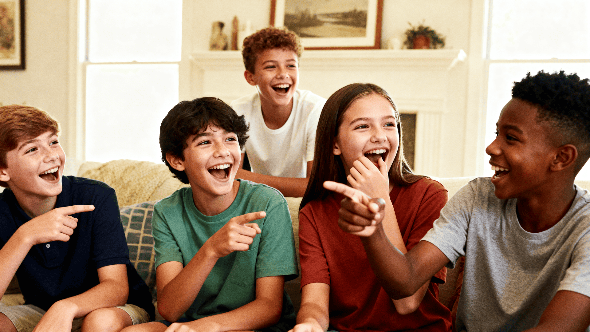 Group of kids laughing, pointing, and playing a fun game together on a couch in a bright, cozy living room setting