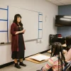 Teacher standing by whiteboard in classroom with students seated at desks