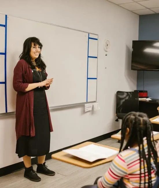Teacher standing by whiteboard in classroom with students seated at desks