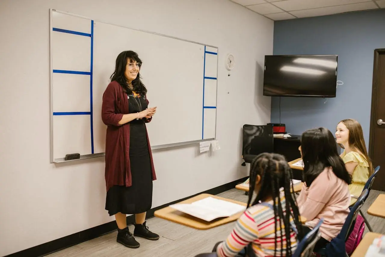Teacher standing by whiteboard in classroom with students seated at desks