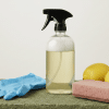 Homemade cleaning spray bottle with gloves, sponge, and lemons on a surface