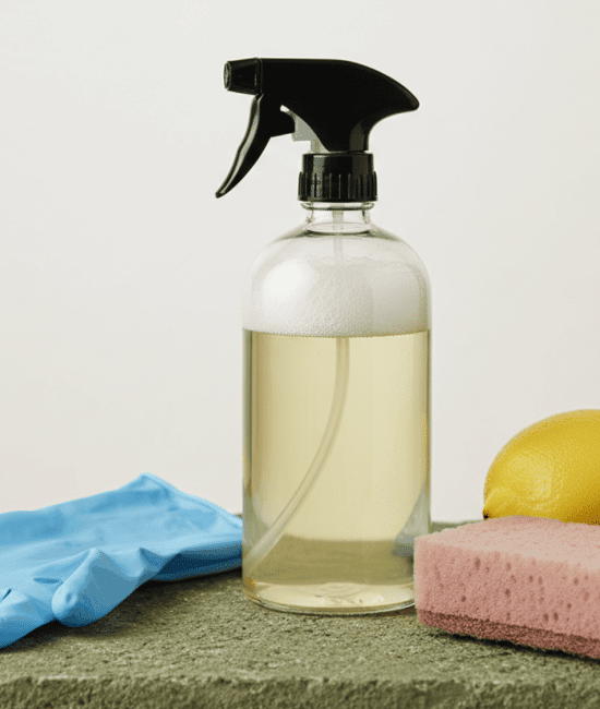 Homemade cleaning spray bottle with gloves, sponge, and lemons on a surface